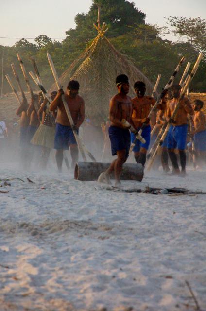 Índio saltando com vara sobre uma tora no chão