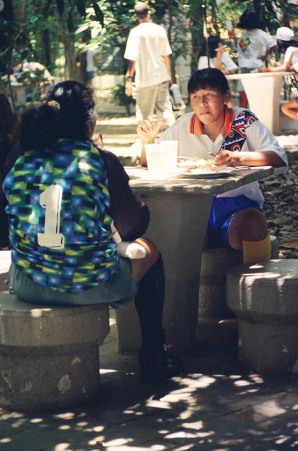 Indígenas conversando à mesa de uma praça