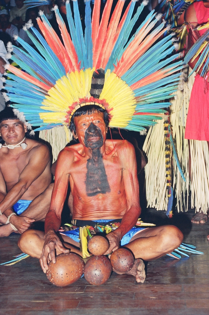 Idoso indígena com cocar e instrumentos