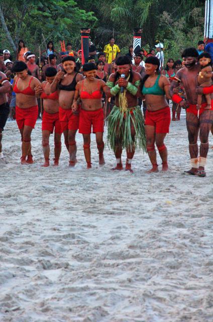 índio com microfone no centro da arena, de braços dados com outros índios